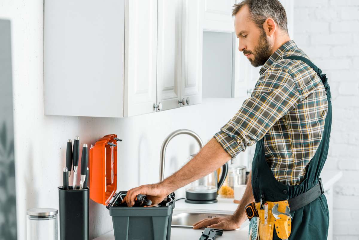 Side view of handsome plumber taking tools from toolbox in kitchen (R) (S)